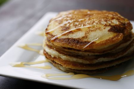 A stack of delicious golden pancakes with honey on a white plate.の写真素材