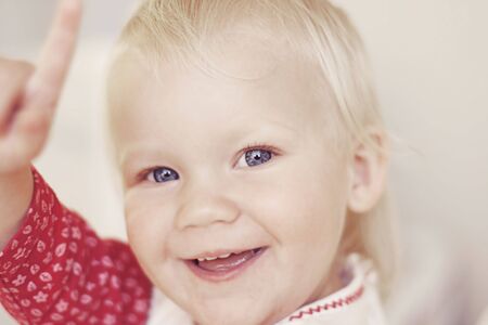 A close-up portrait of a cute smiling and laughing toddler pointing upwards.