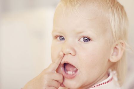 A close-up portrait of a cute little girl pointing at her nose.の写真素材