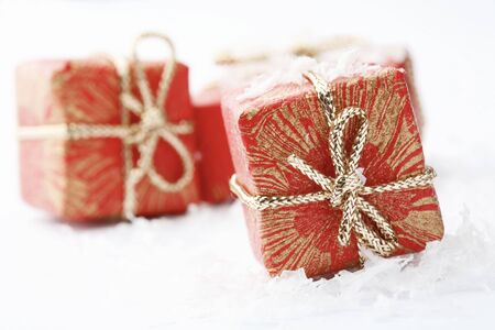 A close-up of Christmas gifts with red wrapping and decorative bows resting on white snowflakes.の写真素材