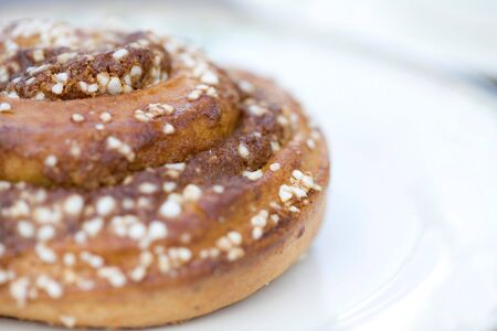 A close-up of a round scroll shaped sweet pastry bun with white icing sugar sprinkles on a white saucer.の写真素材