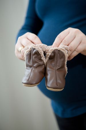 Pregnant mother holding cute little leather baby booties in front of her round tummyの写真素材