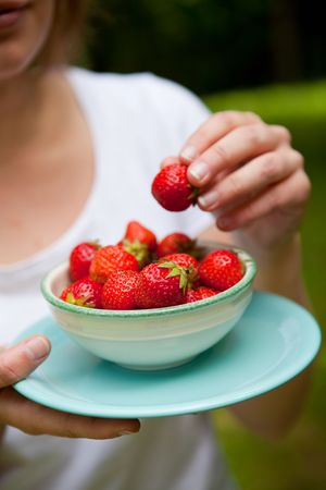 Girl holding a bowl of beautiful fresh strawberries outdoors on a summer dayの写真素材
