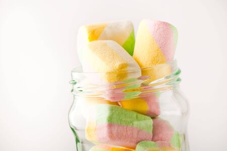 Soft, fluffy, colorful marshmallow in a glass jar on a white backgroundの写真素材