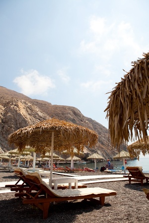Beach umbrellas and sunbeds in morning sun in Perissa beach, Santorini, Greeceの写真素材