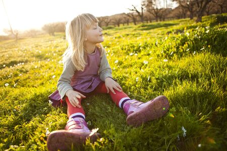 Cute little girl outdoors on a green field with flowersの写真素材