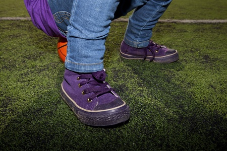 Closeup of a child sitting on a basketball with jeans and sneakers on an outdoor court