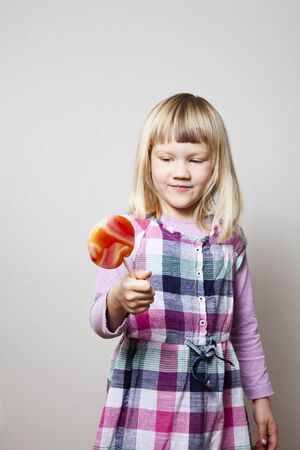 Cute little girl with a big orange lollipop. Studio shot.の写真素材