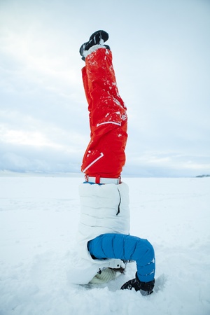 Woman doing yoga and a headstand in snow on a white winter dayの写真素材