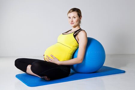 Pregnant woman relaxing while leaning against a fitness ball on a mat in a sitting positionの写真素材