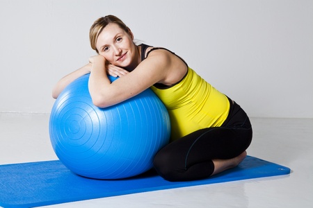 Pregnant woman relaxing while leaning against a fitness ball on a mat in a kneeling positionの写真素材