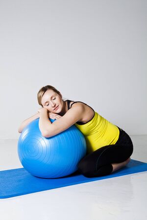 Pregnant woman relaxing while leaning against a fitness ball on a mat in a kneeling positionの写真素材