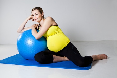 Pregnant woman relaxing while leaning against a fitness ball on a matの写真素材