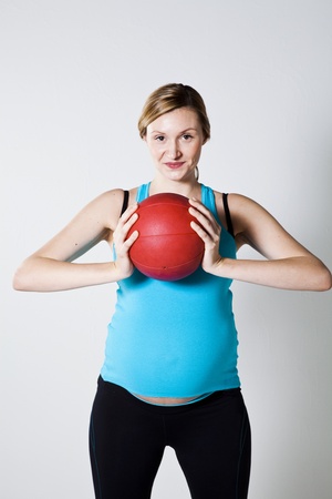 Pregnant woman holding a red exercise ball next to her chestの写真素材