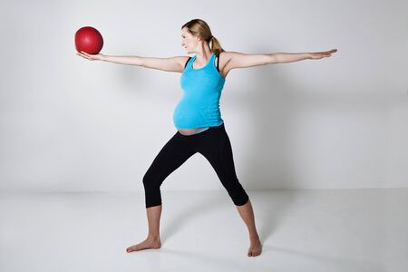 Pregnant woman exercising with an exercise ball held in raised handの写真素材