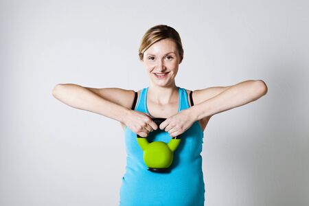 Pregnant woman doing shoulder muscle strengthening exercise with kettlebellの写真素材