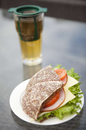 Close-up of a ham, cheese and tomato sandwich made with rye bread  Glass of green tea on the backgroundの写真素材