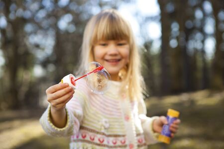 Little girl in cute clothes blowing bubbles outdoorsの写真素材