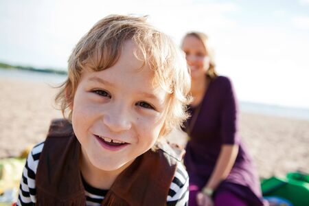 Portrait of a happy boy at the beach with his mother in the background.の写真素材