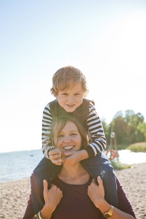 Mother carrying son on shoulders and having fun together at the beach.の写真素材