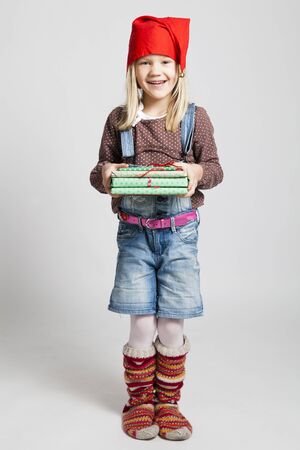 Studio portrait of happy smiling young girl with red Christmas hat and woollen socks holding Christmas giftsの写真素材
