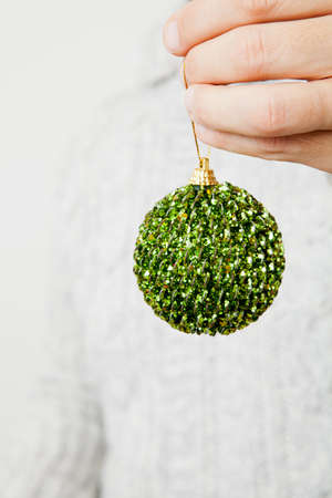 Closeup of green Christmas bauble hanging from fingersの写真素材