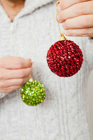 Closeup of red and green Christmas baubles hanging from fingersの写真素材