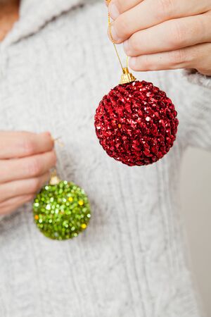 Closeup of red and green Christmas baubles hanging from fingersの写真素材