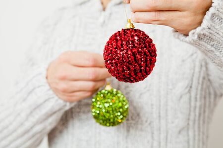Closeup of red and green Christmas baubles hanging from fingersの写真素材