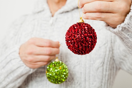 Closeup of red and green Christmas baubles hanging from fingersの写真素材