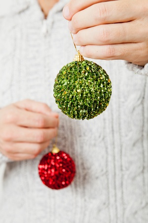 Closeup of red and green Christmas baubles hanging from fingersの写真素材