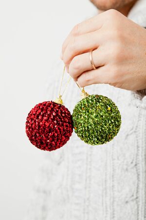 Closeup of green and red Christmas baubles held my man wearing gold wedding ringの写真素材
