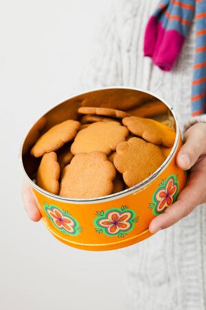 Tin of gingerbread biscuits being held up and presented by man wearing scalfの写真素材
