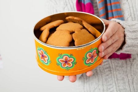 Tin of gingerbread biscuits being held up and presented by man wearing scalfの写真素材
