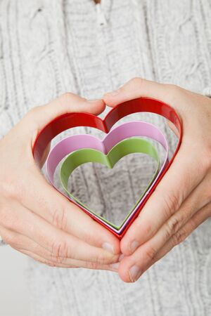 Three colored metal heart symbols held in the hands of a manの写真素材