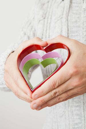 Three colored metal heart symbols held in the hands of a manの写真素材