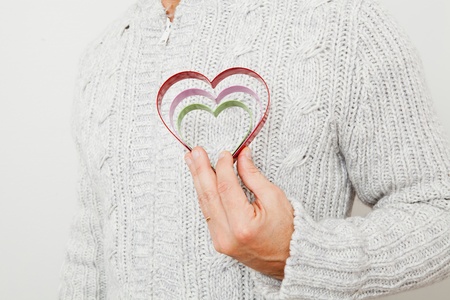 Three colored metal heart symbols held in the hand of a man wearing a gold wedding ringの写真素材