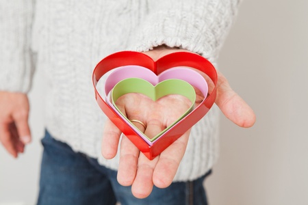 Three colored metal heart symbols held in the hand of a man wearing a gold wedding ringの写真素材