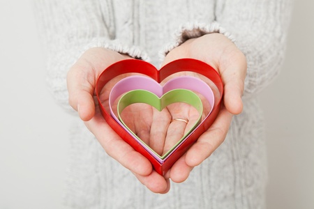 Three colored metal heart symbols held in the hand of a man wearing a gold wedding ringの写真素材
