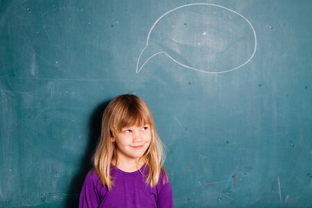 Portrait of young girl looking at empty idea bubble drawn on chalkboardの写真素材