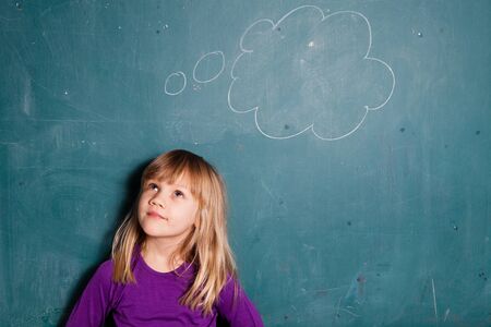 Portrait of young girl looking at empty idea bubble drawn on chalkboardの写真素材