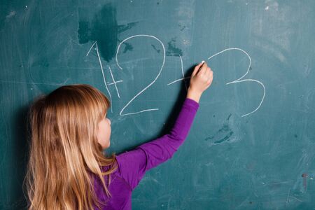 Young girl writing numbers on chalkboard with chalkの写真素材