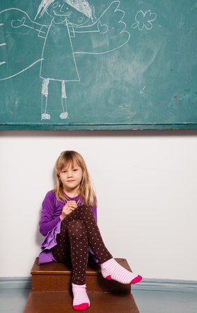 Studio portrait of relaxed young girl in classroom sitting in front of chalkboard with drawing of angelの写真素材