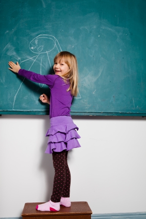 Studio portrait of smiling happy young girl in classroom drawing on a chalkboardの写真素材