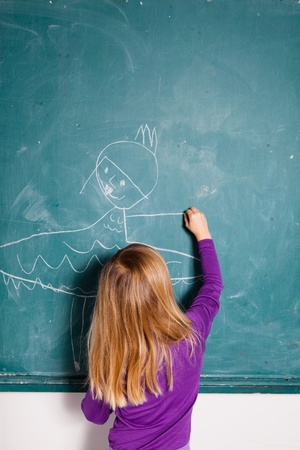 Studio portrait of young girl in classroom drawing image of girl in dress on a chalkboardの写真素材
