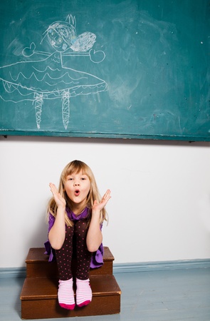 Studio portrait of young girl sitting in classroom in front of chalkboard with drawing and blowing kissの写真素材