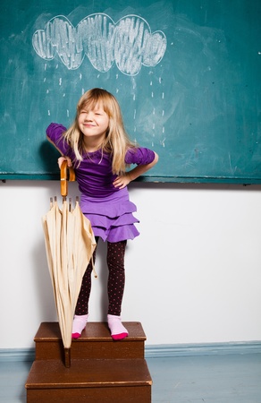 Studio portrait of smiling young girl holding an umbrella while standing in front of chalkboard with image of rain cloudの写真素材
