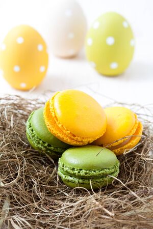 Close-up of colorful macaroons resting in straw nest and Easter eggs on light backgroundの写真素材