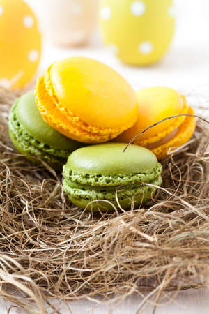 Close-up of colorful macaroons resting in straw nest and Easter eggs on light backgroundの写真素材
