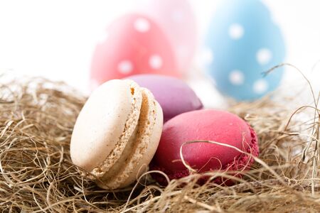 Close-up of colorful macaroons resting in straw nest and Easter eggs on light backgroundの写真素材